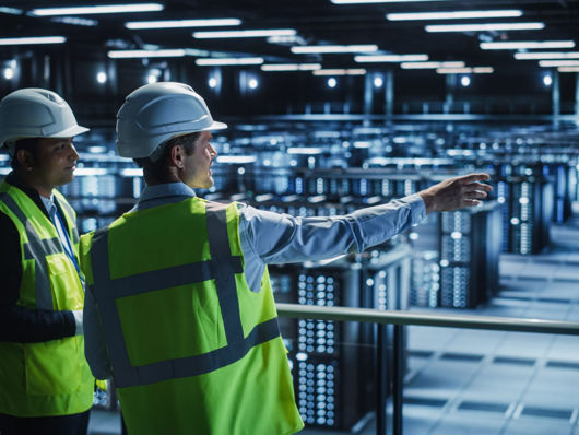 Two people in conversation overlooking a data centre   